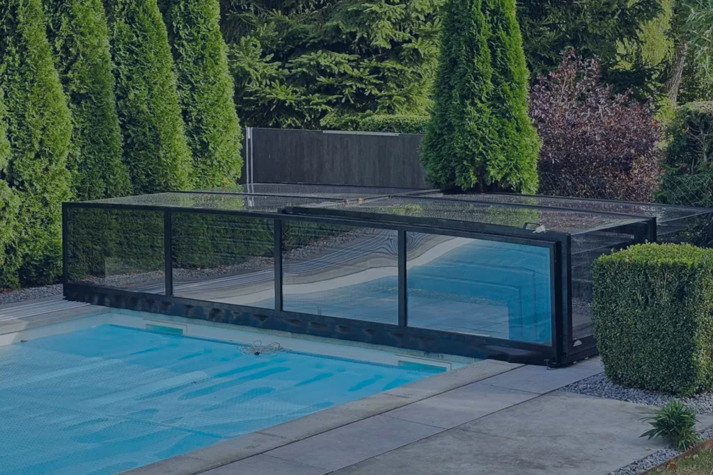 Zadaszenie basenu z przezroczystymi panelami, otoczone zielonymi krzewami.