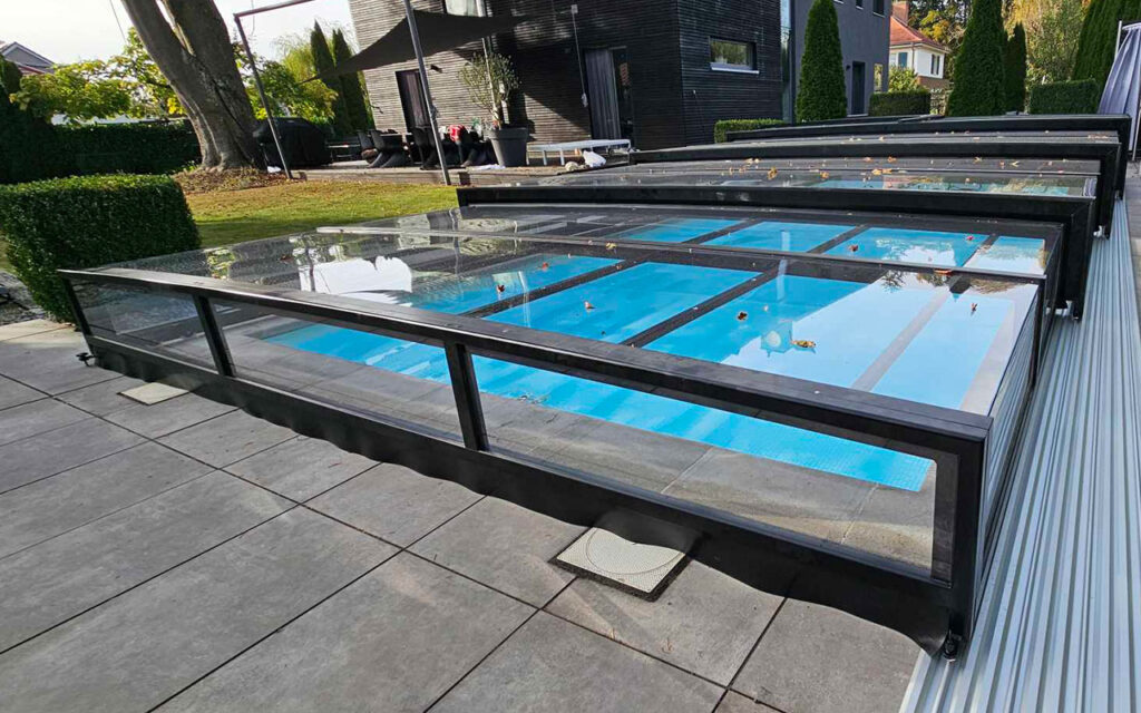 Przesuwne zadaszenie basenowe z przezroczystymi panelami na tle ogrodu.