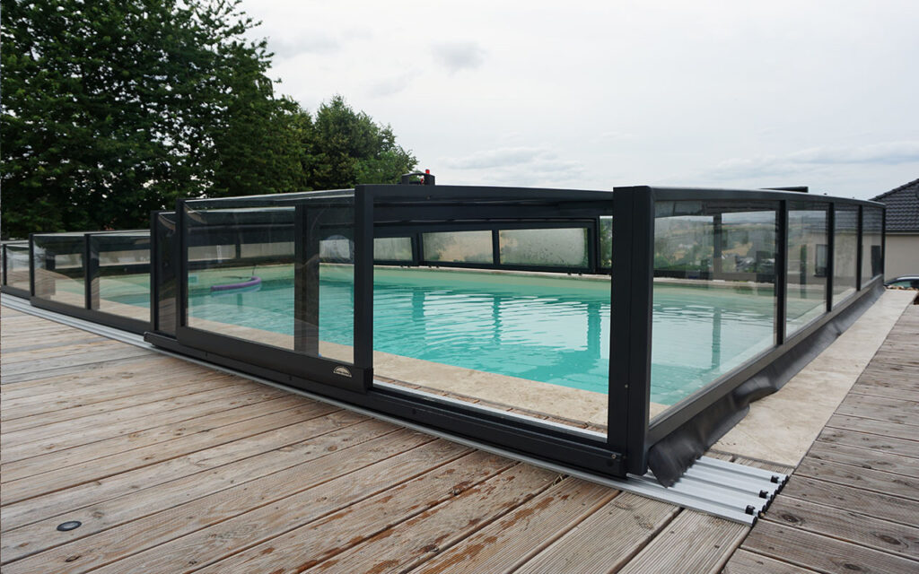 Basen z przesuwanym zadaszeniem na drewnianym tarasie, otoczony zielenią.