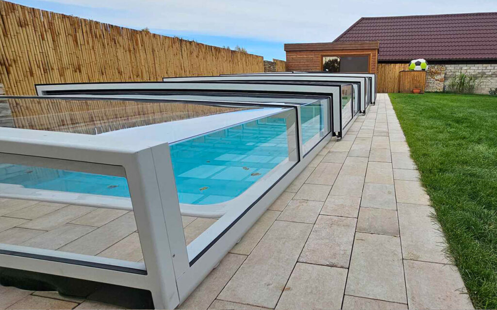 Zadaszenie basenu nad płytkami, obok trawnik i drewniane ogrodzenie.