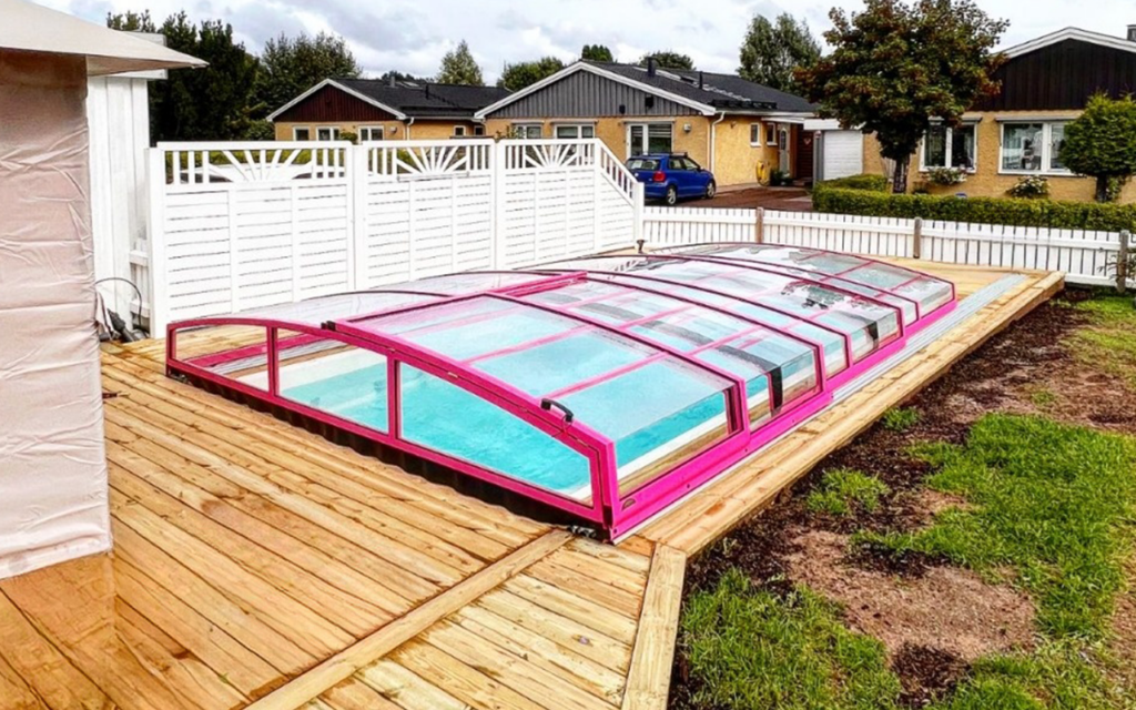 Zadaszenie basenu z różową ramą na drewnianym tarasie, w tle domy i drzewa.