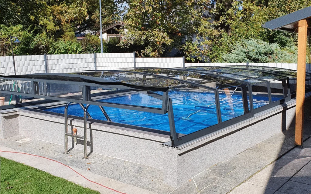 Zadaszenie basenowe nad prostokątnym basenem w ogrodzie, otoczone bujnymi drzewami i krzewami.