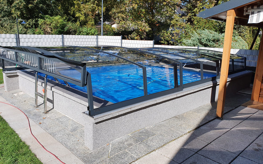 Zadaszenie basenu z przezroczystym panelem na tle ogrodu i drzew.