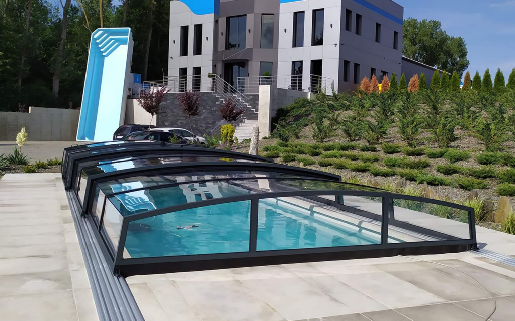 Nowoczesne zadaszenie basenu obok stylowego budynku z ogrodem w tle.