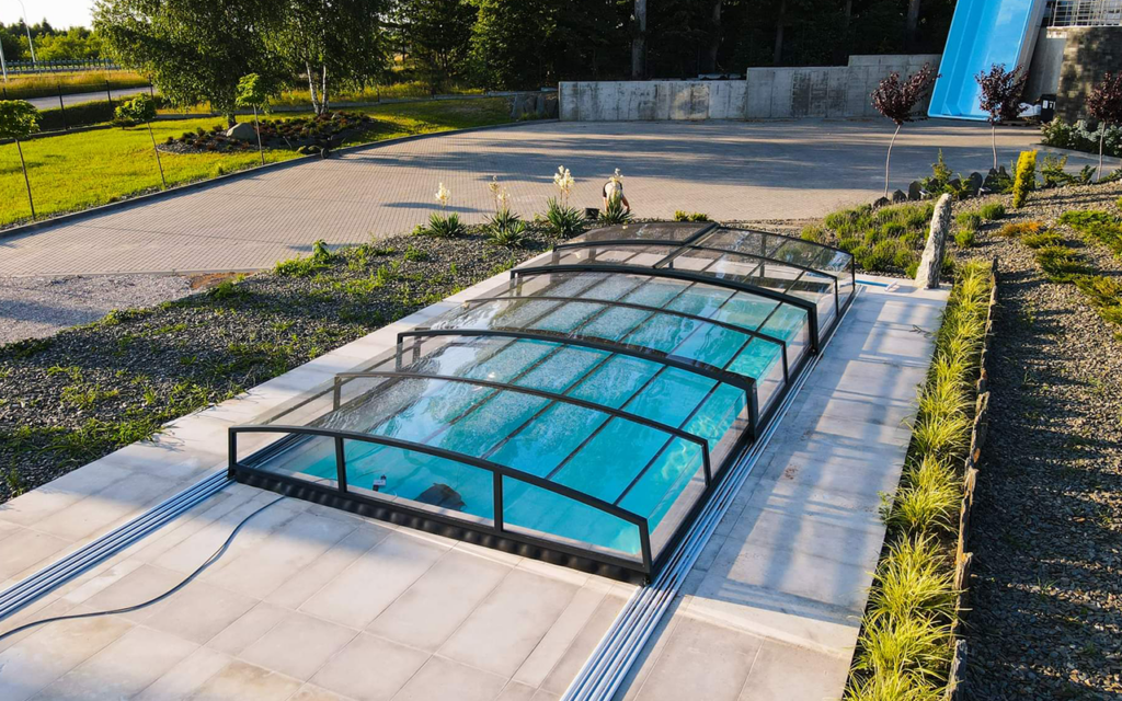 Przesuwane zadaszenie basenu na tle zielonych terenów i roślinności.