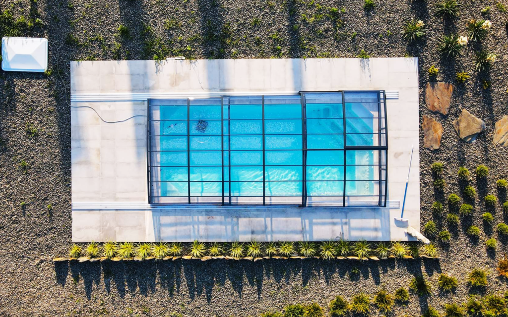 Basen kryty prostokątną osłoną, otoczony żwirkiem i zielenią. Widok z góry.