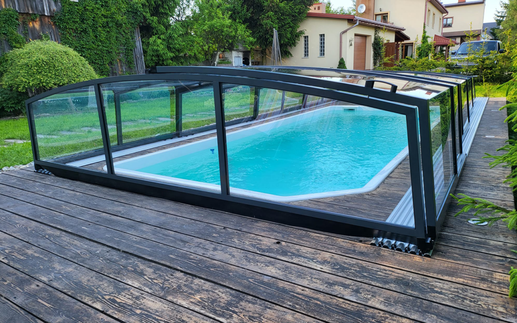 Zadaszenie basenu na drewnianym tarasie w ogrodzie, zielona roślinność w tle.