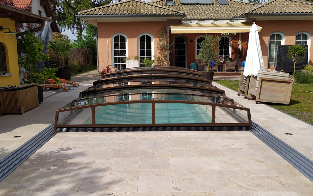 Basen ze szklanym zadaszeniem przy nowoczesnym budynku z tarasem i roślinami.