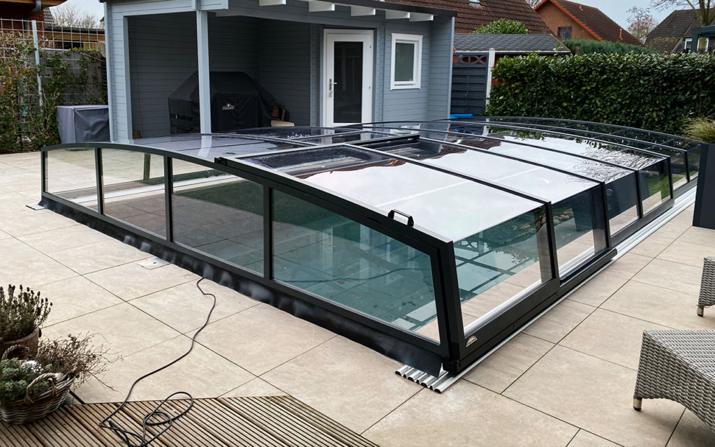 Zadaszenie basenowe z przezroczystymi panelami na tarasie obok altany i roślin.