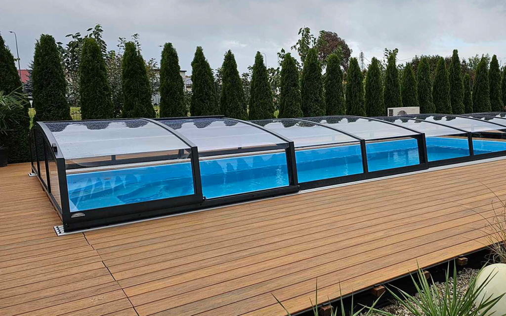 Zadaszenie basenu na drewnianym tarasie, otoczone wysokimi drzewami iglastymi.