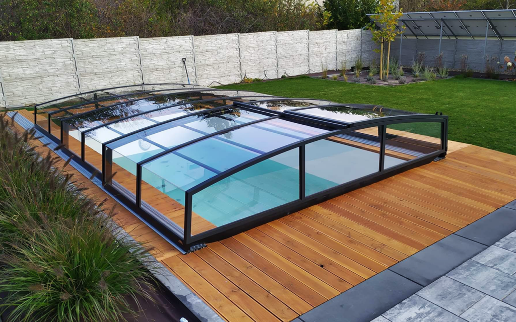 Basen z osłoną w ogrodzie, drewniany taras, zieleń w tle.