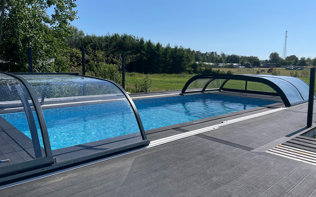 Zadaszenie basenu z przezroczystego materiału, drewniany taras i zieleń w tle.