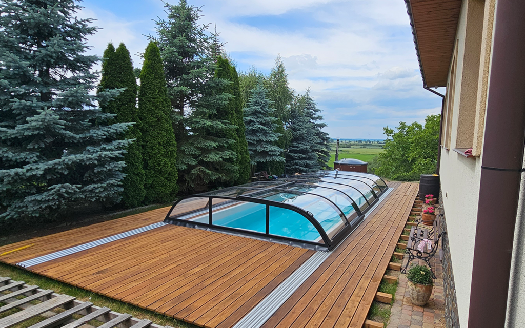 Zadaszenie basenu w ogrodzie otoczone zielonymi drzewami, obok drewniany taras.