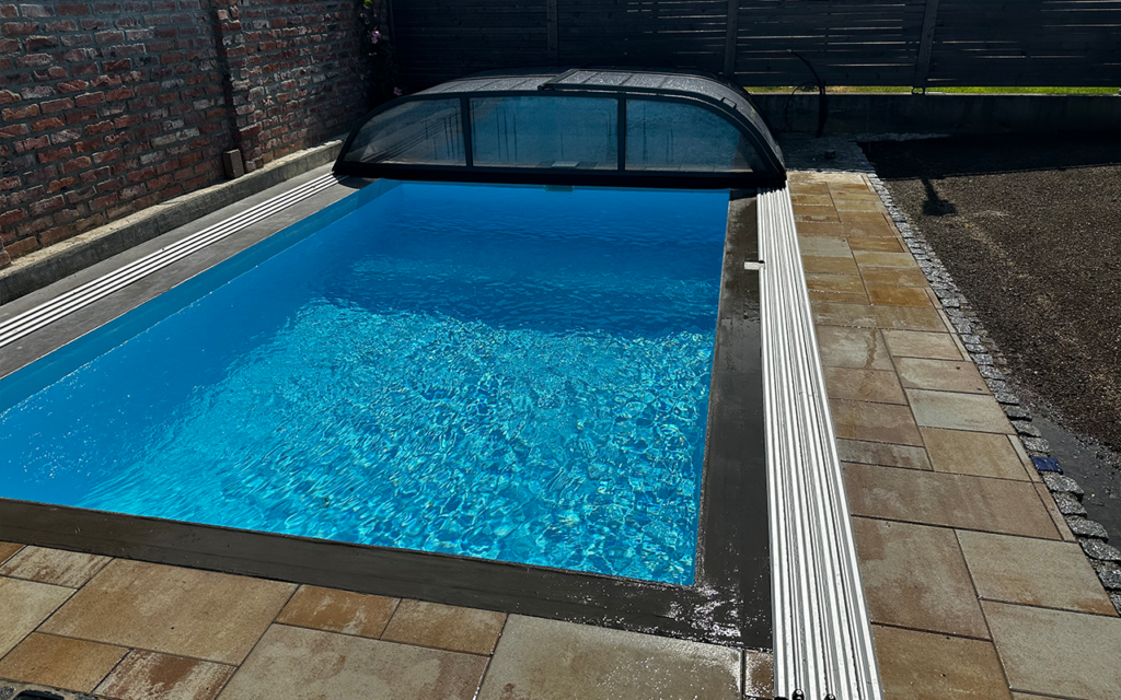 Basen z niebieską wodą, częściowo przykryty przezroczystym zadaszeniem, otoczony płytkami.