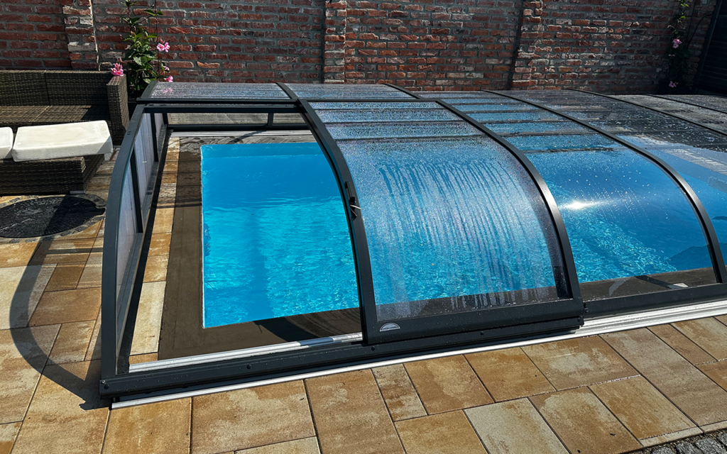 Zadaszenie basenu z przezroczystego materiału na tle ceglanego muru i kamiennej posadzki.