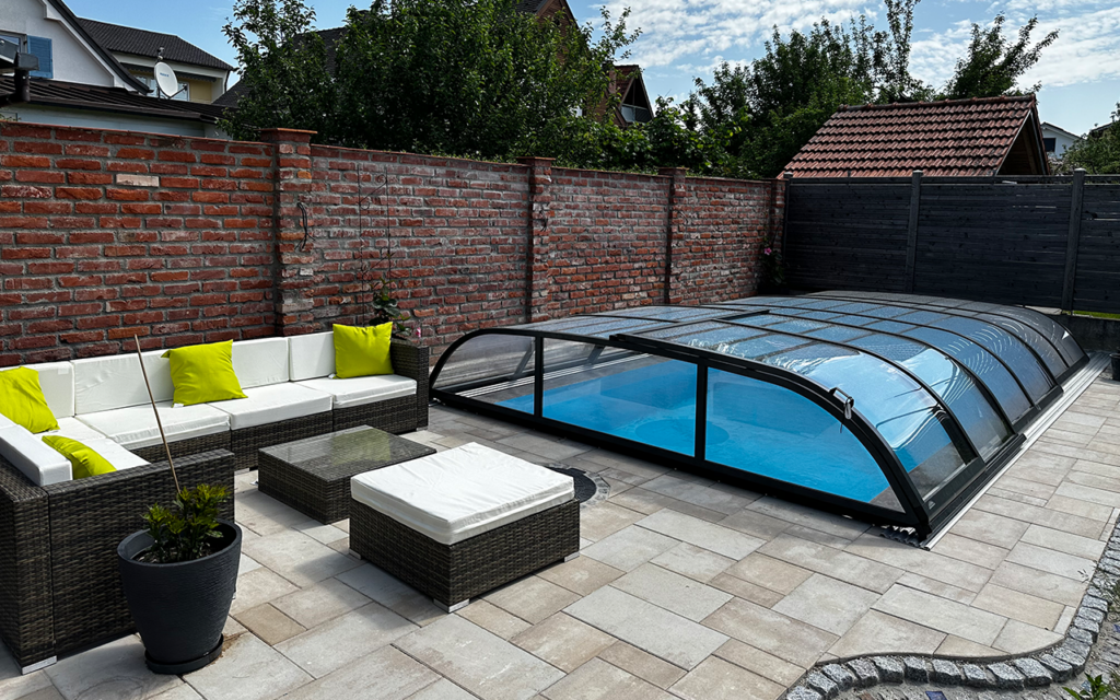 Nowoczesne zadaszenie basenu na tarasie obok zestawu wypoczynkowego z sofą i stolikiem.