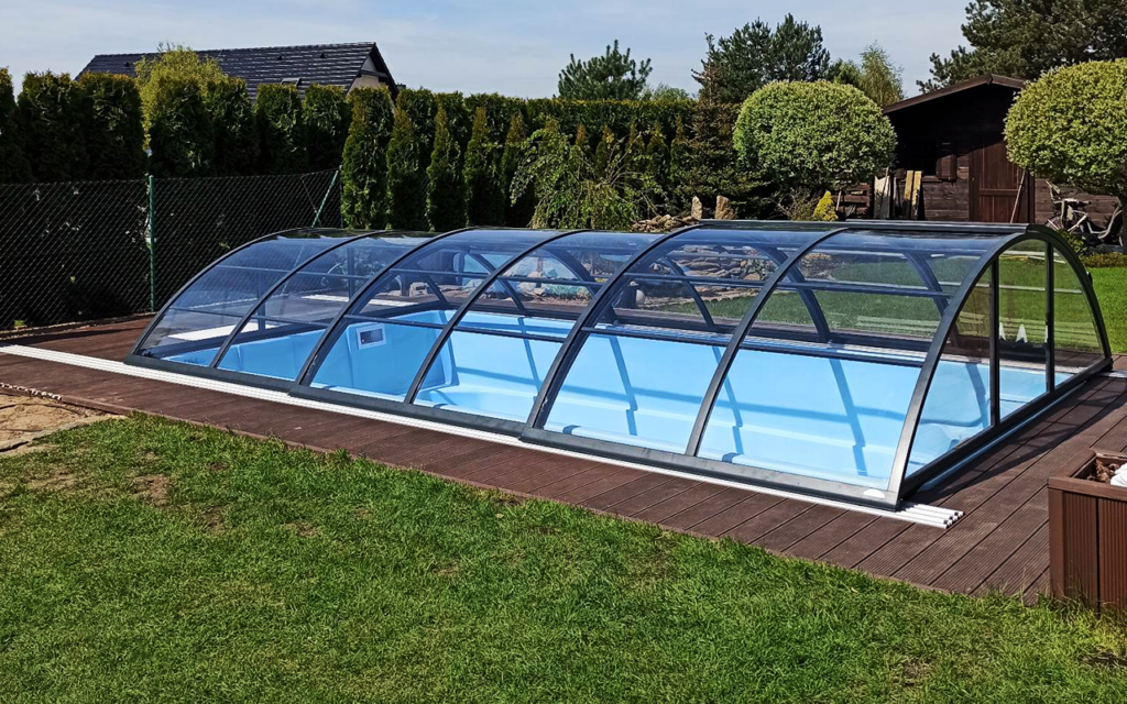 Zadaszenie basenu ogrodowego na drewnianym tarasie, otoczone zielenią i koniczynami.