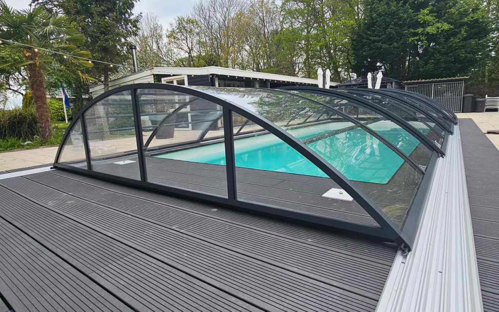 Przeszklona zabudowa basenu na drewnianym tarasie z widokiem na ogród i drzewa.