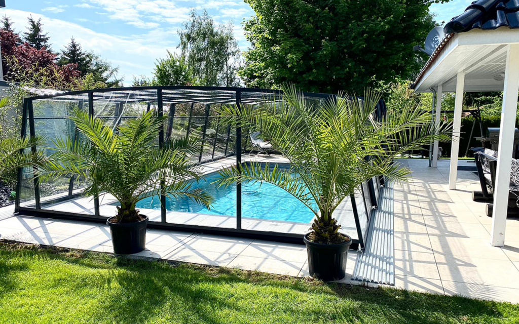 Zadaszenie basenowe z metalową konstrukcją, otoczone roślinnością i trawnikiem, obok zadaszona altana.