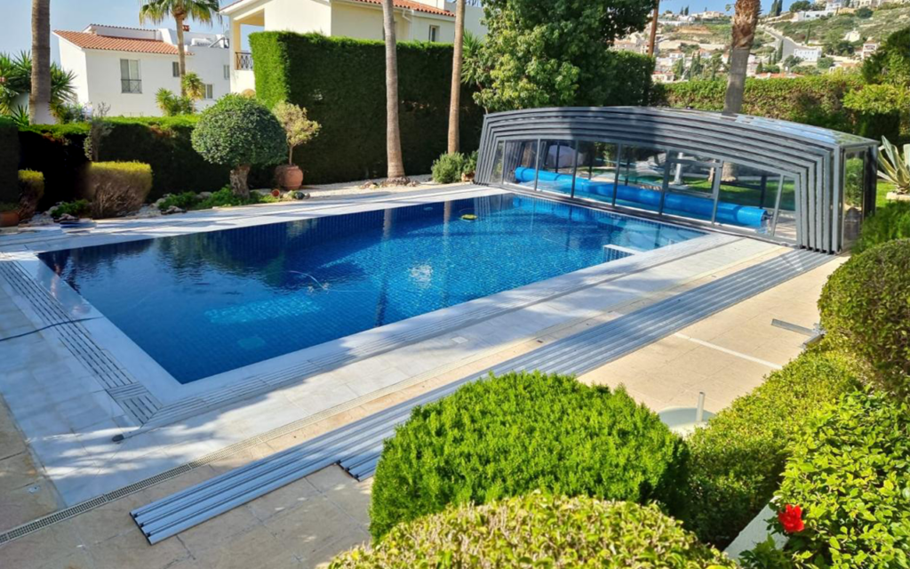 Zadaszony basen z nowoczesnym, przesuwnym zadaszeniem, otoczony bujną zielenią i drzewami w ogrodzie.