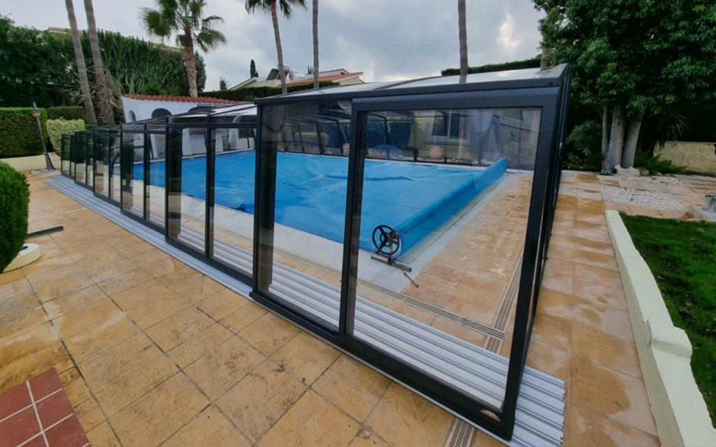 Zadaszenie basenu z przesuwanymi panelami w ogrodzie, otoczone zielenią i palmami.