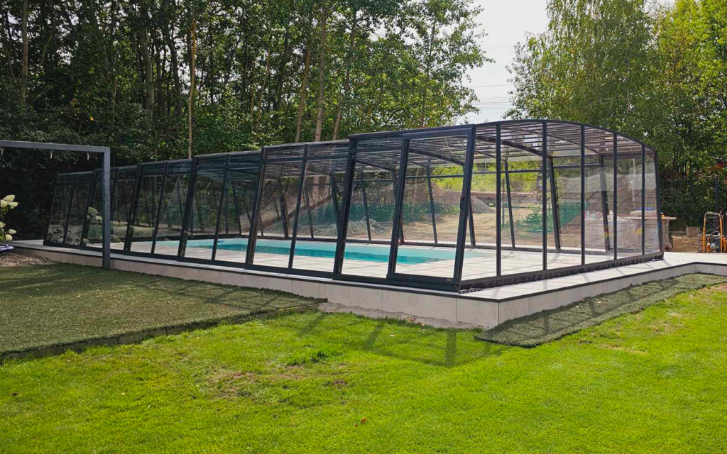 Basen z zadaszeniem aluminiowym w otoczeniu zieleni i drzew.