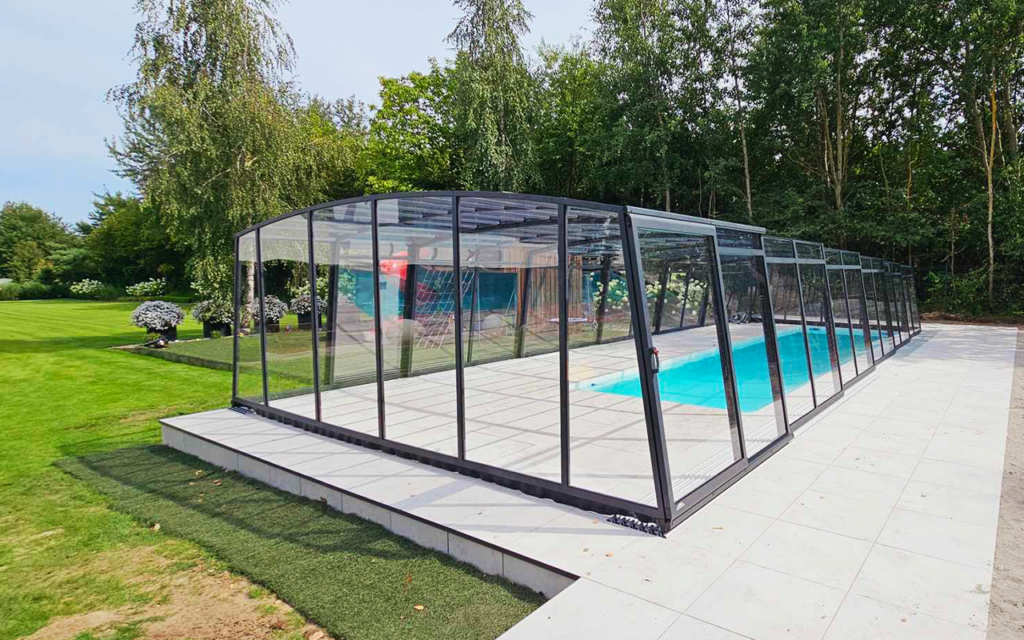 Zadaszenie basenu w ogrodzie, nowoczesna konstrukcja z przezroczystymi panelami, otoczone zielonymi drzewami.